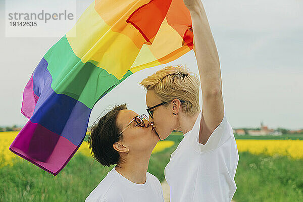 Liebevolle Lesben mit Regenbogenfahne küssen sich