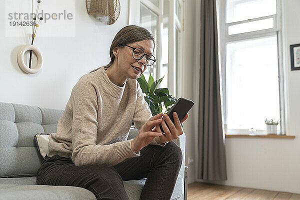 Reife Frau benutzt Smartphone zu Hause auf dem Sofa