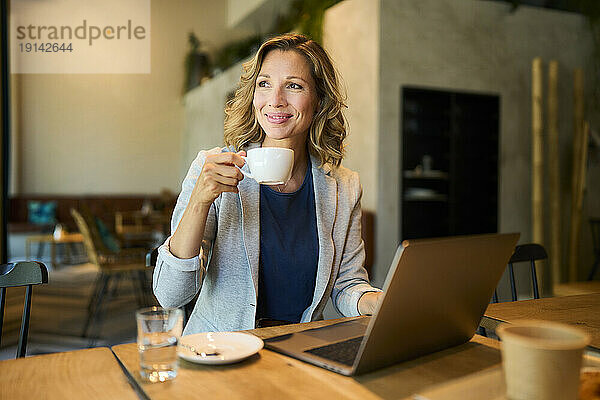 Lächelnde Geschäftsfrau beim Kaffeetrinken mit Laptop im Café