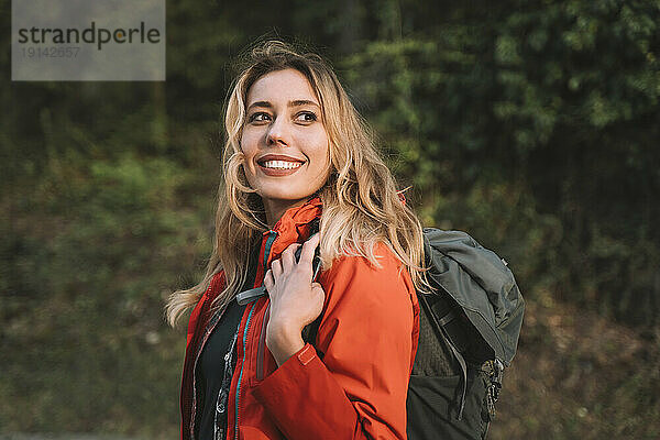 Blonde glückliche Frau mit Rucksack im Wald