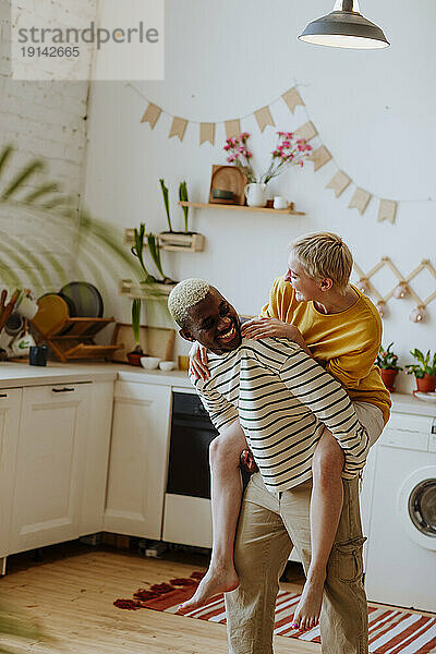 Verspielter Mann huckepack mit seiner Freundin in der heimischen Küche