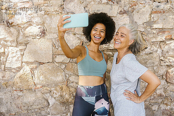 Glückliche Tochter macht Selfie mit Mutter  die vor einer Steinmauer steht