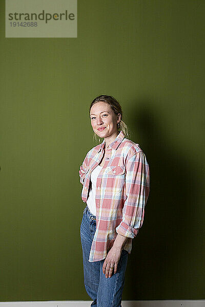 Selbstbewusste junge Frau im karierten Hemd steht vor einer grünen Wand