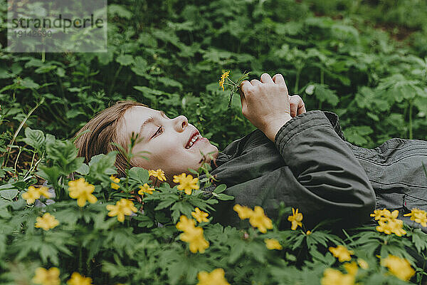 Glückliches Mädchen  das neben gelben Blumen im Wald liegt