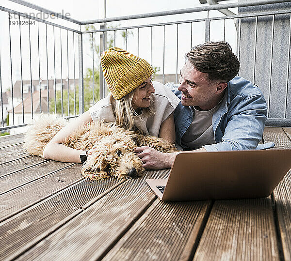 Glückliches Paar liegt mit Laptop und Hund auf dem Boden