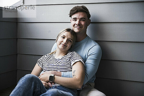 Lächelndes junges Paar sitzt zusammen an der Wand auf dem Balkon