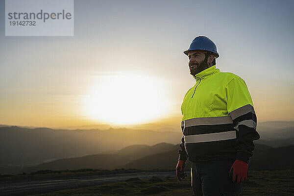 Lächelnder Ingenieur im reflektierenden Anzug bei Sonnenuntergang