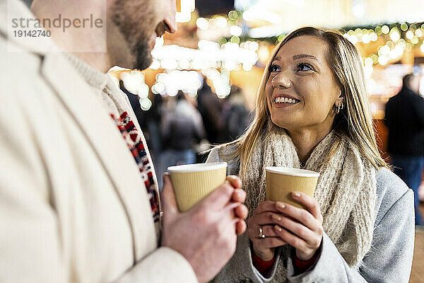 Lächelnde Frau und Mann mit Kaffeetasse auf dem Weihnachtsmarkt