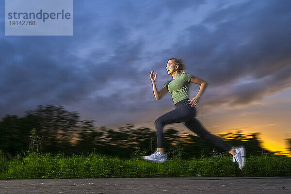 Young athlete sprinting on footpath at dusk