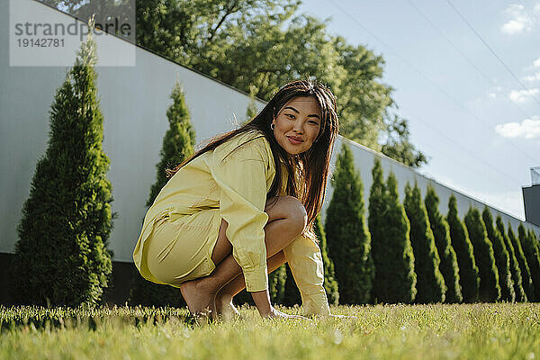 Lächelnde Frau kauert auf Gras im Hinterhof