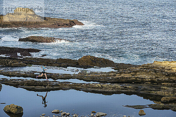 Junge Frau joggt auf Felsen am Meer