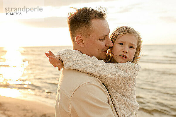Smiling father embracing daughter at sunset