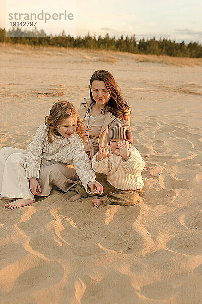 Lächelnde Mutter mit Tochter und Sohn  die am Strand im Sand spielen