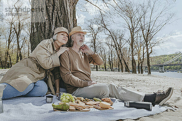 Paar sitzt auf Picknickdecke mit Snacks am Strand