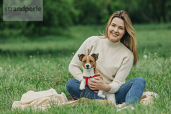 Glückliche junge Frau sitzt mit Jack-Russell-Terrier-Hund im Park