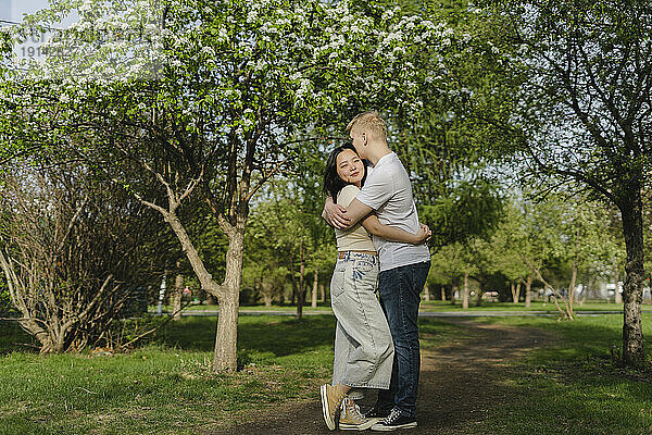Junges Paar umarmt sich an Bäumen im Park