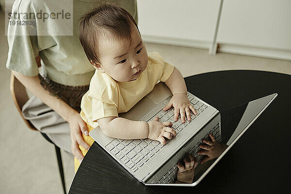 Cute daughter typing on laptop sitting with mother at home