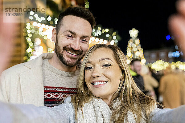 Lächelnde junge Frau macht ein Selfie mit einem Mann auf dem Weihnachtsmarkt