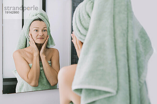 Lächelnde Frau  die Gesichtscreme aufträgt und in den Spiegel schaut