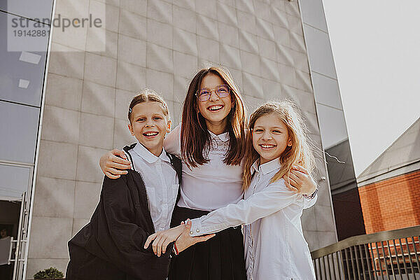 Happy girl with arm around friends standing in front of school building