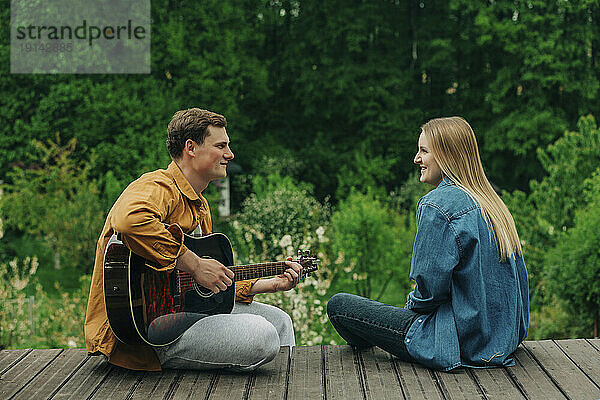 Lächelnde blonde Frau mit Mann  der auf der Promenade Gitarre spielt