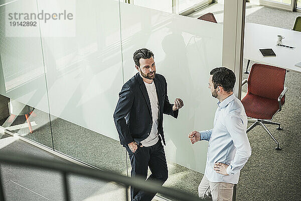 Geschäftskollegen diskutieren darüber  wie sie sich im Büro an eine Glastür lehnen