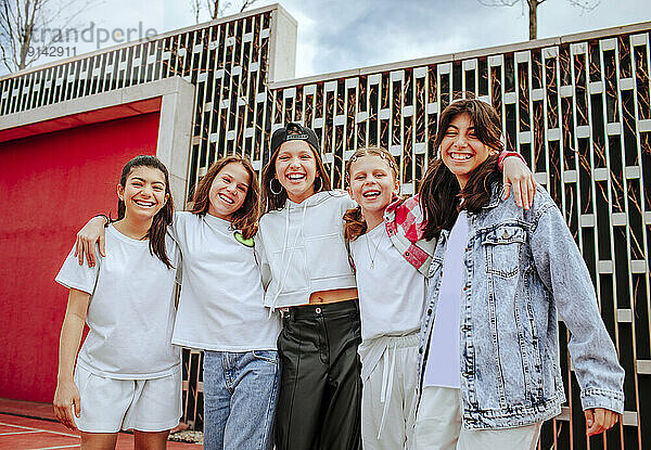 Lächelnde Teenager-Mädchen stehen mit Armen vor der Wand auf dem Spielplatz