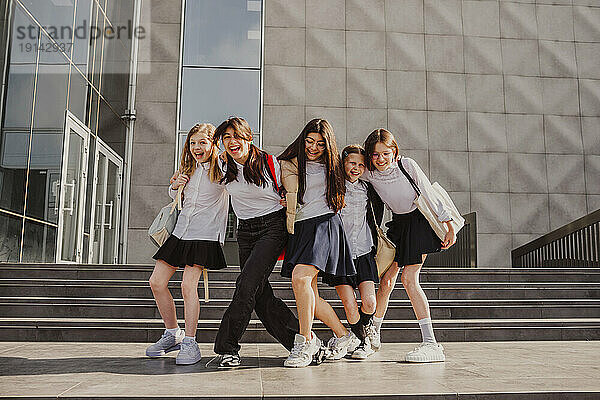 Happy schoolgirls enjoying together standing in front of school building
