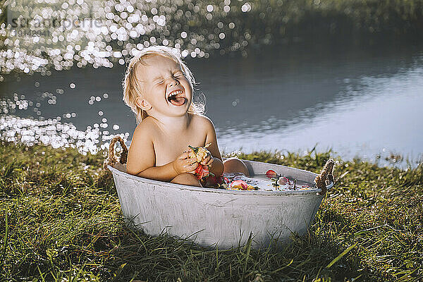 Fröhliches Mädchen  das in der Badewanne am See lacht
