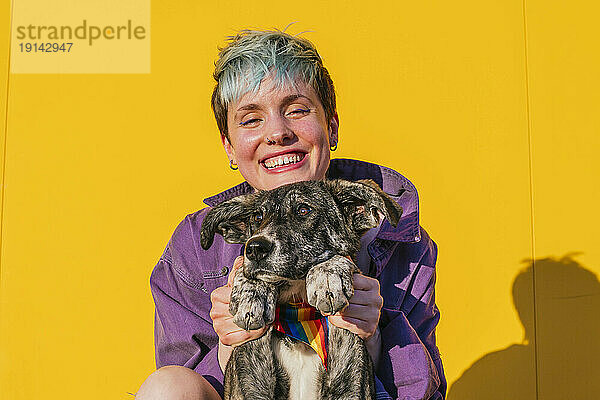 Fröhliche lesbische Frau hält Hundepfote vor gelber Wand
