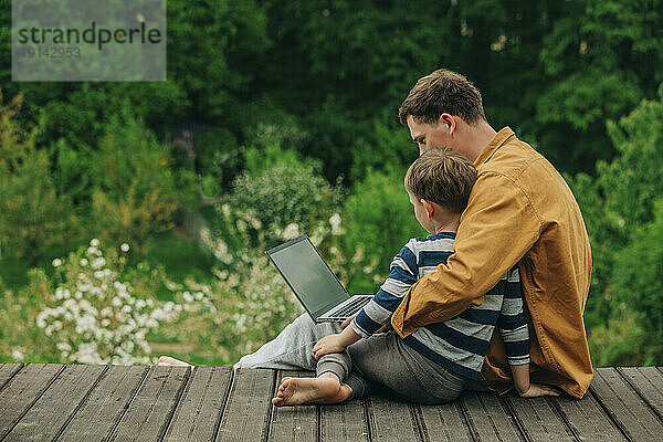 Sohn und Vater benutzen Laptop auf der Promenade