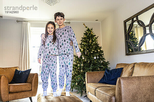 Glücklicher Bruder und Schwester  die zur Weihnachtszeit zu Hause am Tisch im Wohnzimmer stehen