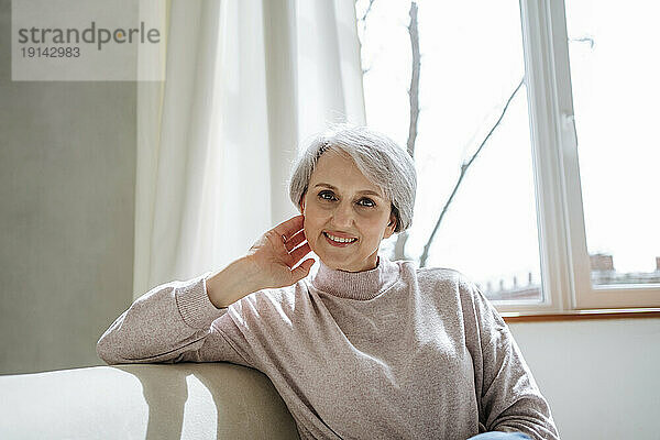 Confident mature woman sitting on couch by window at home