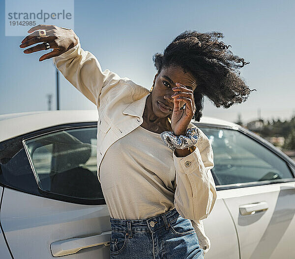 Junge Frau tanzt an einem sonnigen Tag mit einem weißen Auto