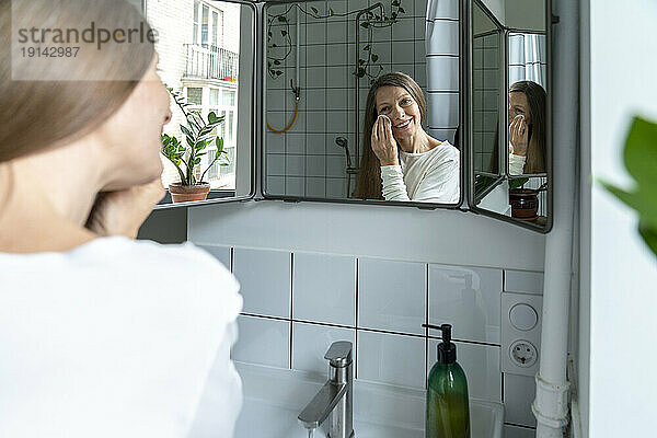 Happy mature woman cleaning face at home