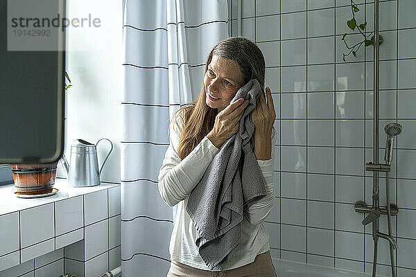 Happy mature woman cleaning face with towel