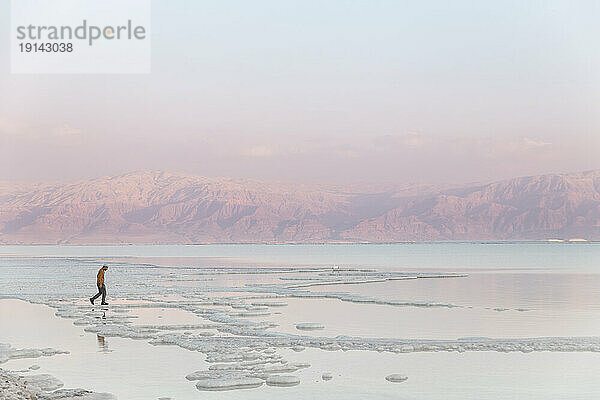 Mann geht bei Sonnenuntergang im Toten Meer auf Salzformationen