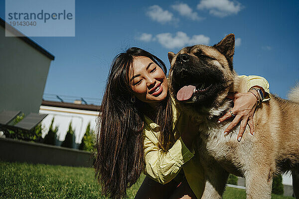 Smiling woman embracing pet dog in back yard