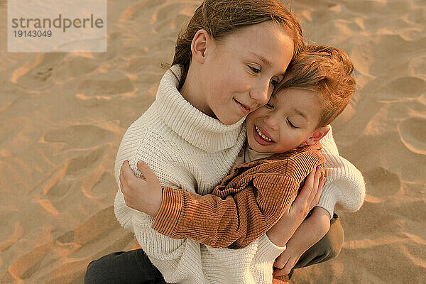 Lächelnde Schwester umarmt Bruder am Strand