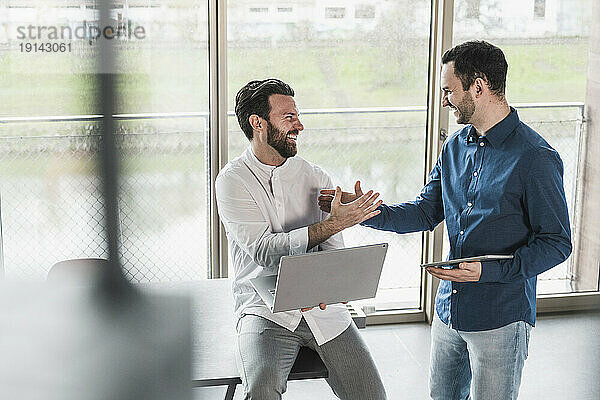 Business colleagues laughing and holding hands in office