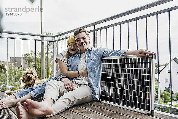 Glückliches Paar sitzt mit Solarpanel und Hund