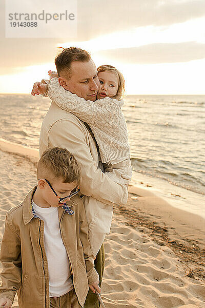 Vater umarmt Tochter und Junge steht am Strand