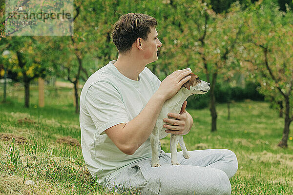 Mann sitzt mit Jack-Russell-Terrier-Hund im Garten