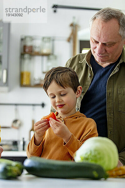 Grandfather watching grandson holding tomato in kitchen