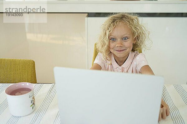 Lächelndes Mädchen  das zu Hause vor dem Laptop ein Gesicht macht