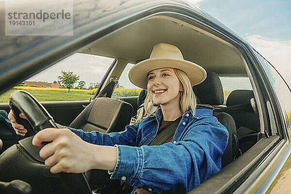 Glückliche Frau  die Auto fährt und durch das Fenster gesehen wird