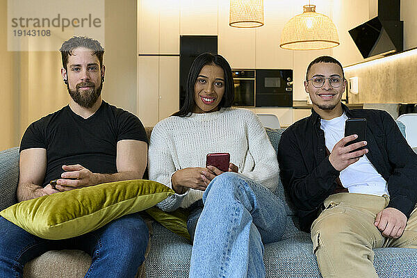 Lächelnde Freunde mit Smartphones sitzen zu Hause auf dem Sofa
