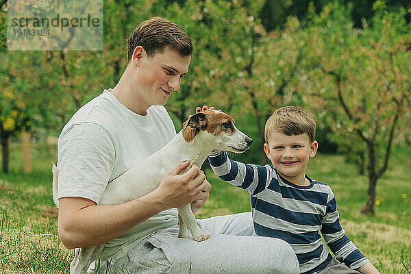 Glücklicher Vater und Sohn streicheln den Hund Jack Russell Terrier im Garten