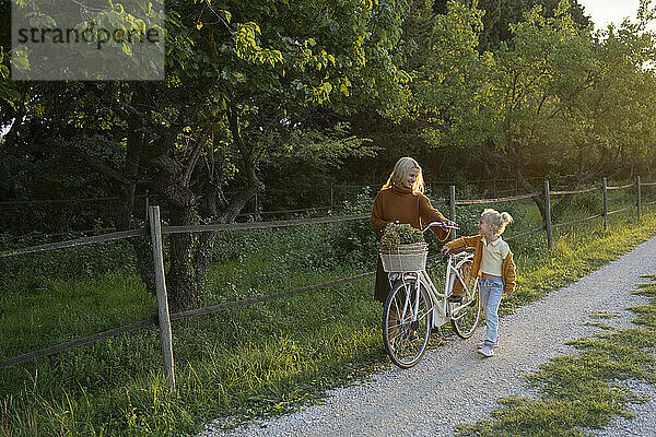 Mutter und Tochter radeln bei Sonnenuntergang mit dem Fahrrad auf dem Fußweg