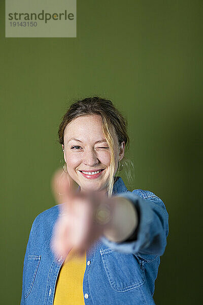 Smiling woman gesturing in front of green wall